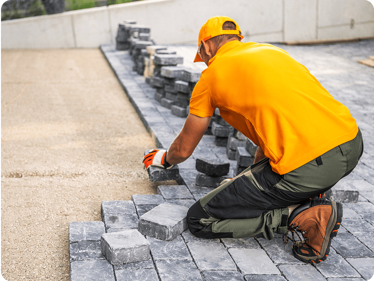 Worker laying paving stones in construction site.